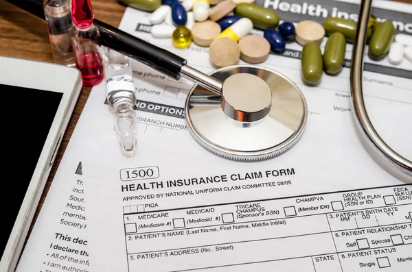 personal health insurance claim form with pills, syringe, mobile phone, stethoscope