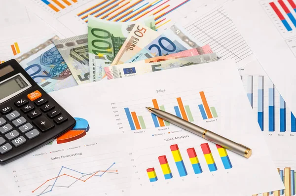 money, calculator, pen on financial paper graphs