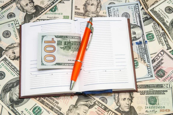 pen lying  on open notebook with dollars background