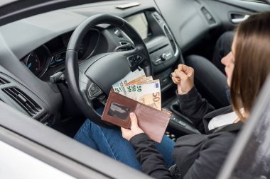 Cüzdanında euro banknotları olan bir kadın arabada oturuyor.