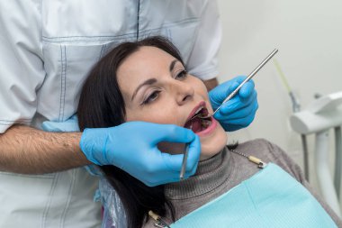 Doktor, dişçilik aletleriyle hastanın dişlerini muayene ediyor.