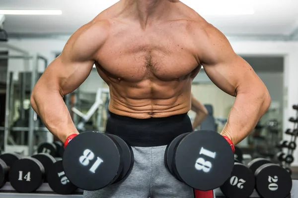 Spor salonunda dambıllarla çalışan bir sporcu.
