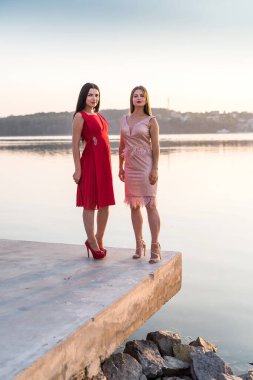 Göl kıyısında poz veren zarif elbiseli iki kadın.