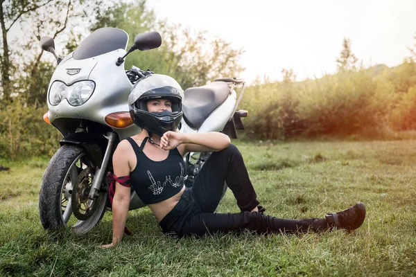 Woman with helmet sitting on the grass near motorcycle