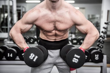 Spor salonunda dambılla çalışan genç bir adam.