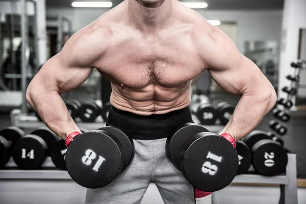 Spor salonunda dambılla çalışan genç bir adam.