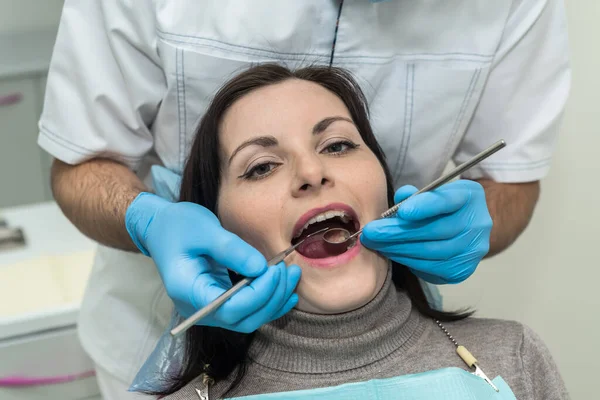 歯医者は歯科の道具で患者の歯を調べる — ストック写真