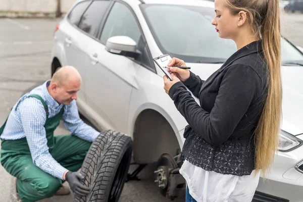 Frau Füllt Dokument Aus Während Mechaniker Rad Wechselt — Stockfoto