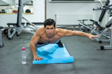 Genç ve sportif bir adam spor salonunda tahta egzersizi yapıyor.