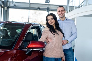Şov salonunda yeni arabalarla poz veren mutlu çift.