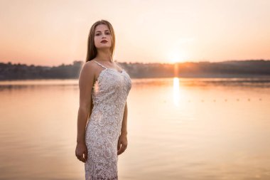 Gün batımında kumsalda zarif elbiseli güzel bir kadın.