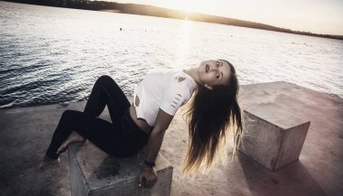 Gölün kıyısında taşın üzerinde oturan kadın.