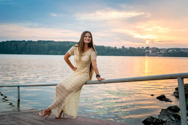 Young beautiful woman against sunset on the lake