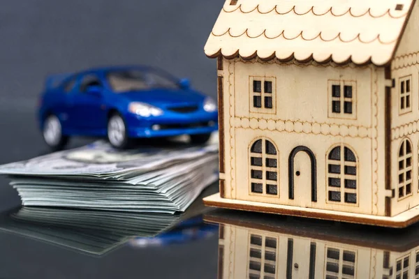 Wooden house model with toy car and dollar pile