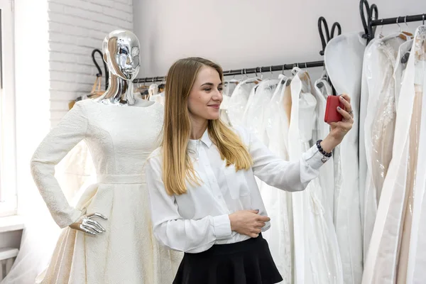 Gelinlik mağazasında mankenle selfie çeken bir kadın.