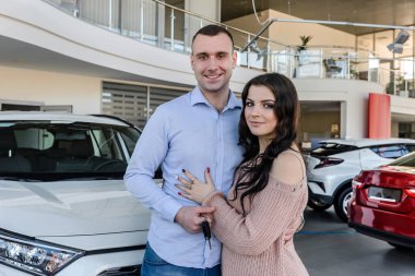 Şov salonunda yeni arabalarla poz veren mutlu çift.