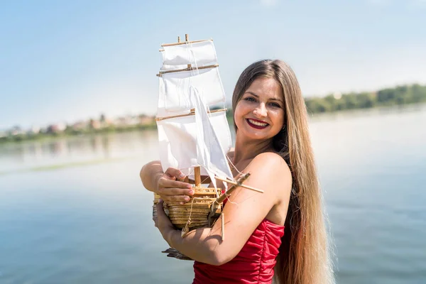 Woman in red dress holding boat model on the beach