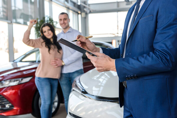 Руки дилера с планшетом и счастливая семья позади