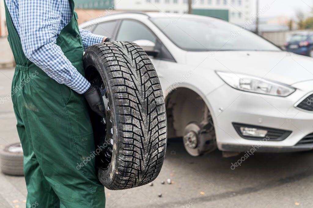 Worker holding spare wheel upon of broken car