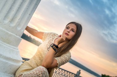 Kadın iskelede oturuyor, suya ve günbatımına karşı