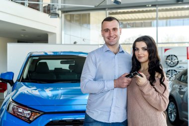 Şov salonunda yeni arabalarla poz veren mutlu çift.