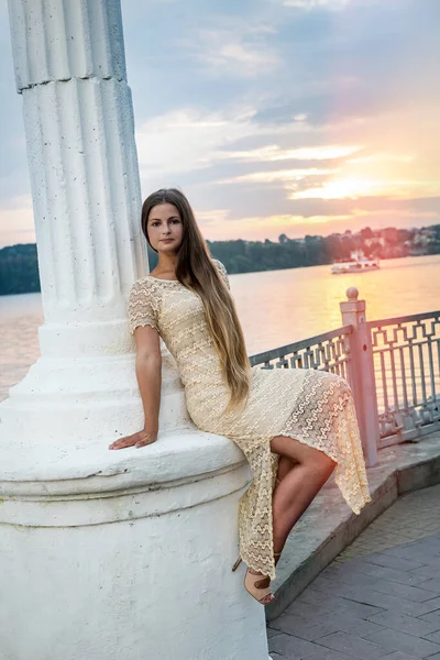 Woman posing sitting on column on lake shore. Urban landscape