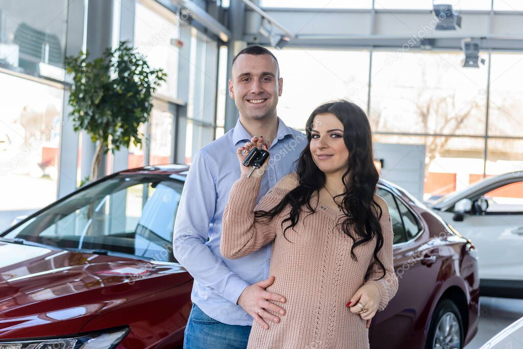 Happy couple posing with keys from new car 