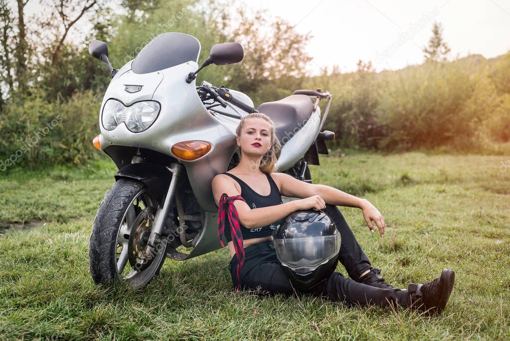 Woman biker sitting near motorcycle with helmet in her arms
