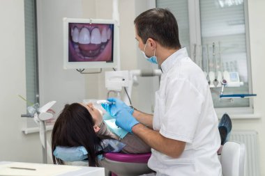 Diş hekimi kamerayla hastanın dişlerini kontrol ediyor, ekrana bakıyor.