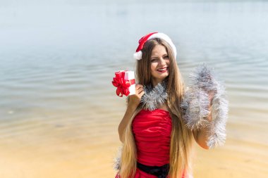 Kırmızı elbiseli, hediye kutusu ve Noel çelengi takan güzel bir kadın.