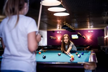 Güzel bir kadın ve arkadaşı barda bilardo oynuyorlar.