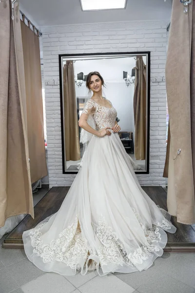 Attractive young bride choosing wedding dress in wedding salon