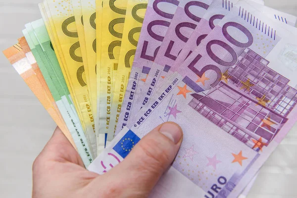 Hand with euro banknotes upon white brick wall close up