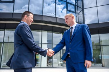 Zarif iş arkadaşları dışarıda el sıkışırken takım elbise giyerler.