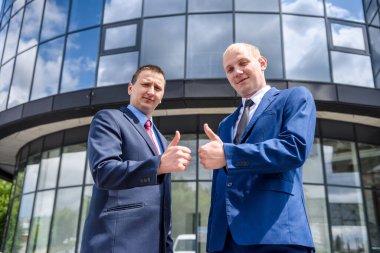 Dışarıda iki takım elbiseli adam baş parmağını kaldırıyor.