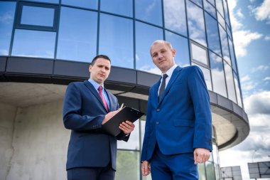 İki ciddi iş adamı iş merkezine karşı poz veriyor.