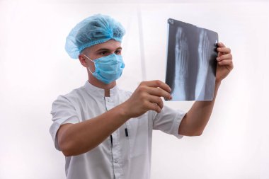 Doktor hastanın röntgenini inceliyor. Mavi üniformalı genç adamın elinde ayak röntgeni var ve ona bakıyor.