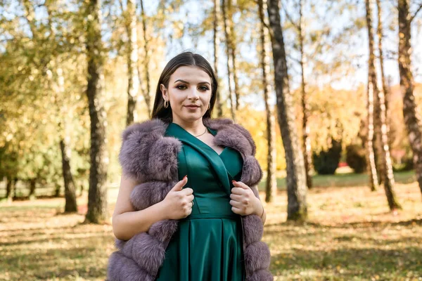 秋の公園を歩いてファッショナブルな緑のドレスを身に着けている若い女性 — ストック写真