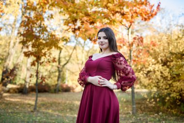 Parkta güzel kırmızı elbiseli genç prenses. Arka plan parlak, altın sonbahar doğası..