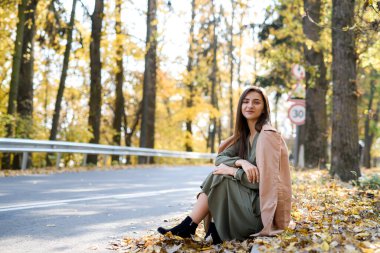 Sonbahar renkleri. Yol kenarında ormanda poz veren ceketli güzel bir kadın.