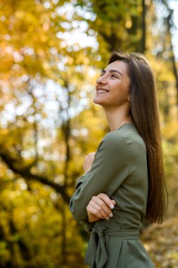 Sonbahar parkında poz veren yeşil elbiseli esmer kadının portresi.