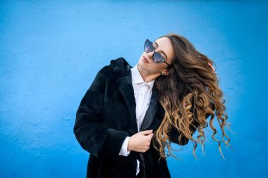 Mavi duvar arkasında kürklü genç bayan. Güzellik ve moda.