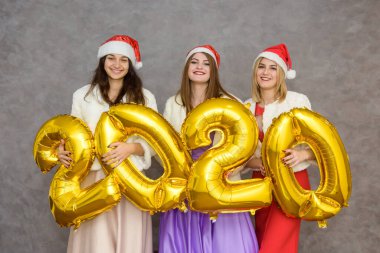 Noel Baba şapkalı üç neşeli kız 2020 numaralı balonlarla parti kutlamalarında poz veriyor.