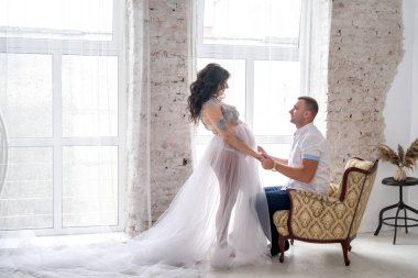 Beklerken. Moda kıyafetleri içinde mutlu hamile çift stüdyoda poz veriyor.