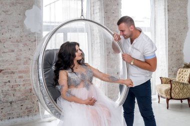 Beklerken. Moda kıyafetleri içinde mutlu hamile çift stüdyoda poz veriyor.