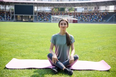 Kadın dışarıda antrenman yapıyor. Yeşil çimlerin üzerinde oturuyor ve yoga egzersizleri yapıyor.