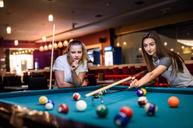 Bilardo oynayan iki kadın ıstaka rafı kullanıyor.