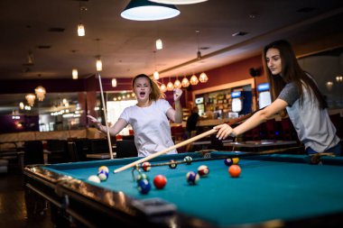 Bilardo oynayan iki kadın ıstaka rafı kullanıyor.