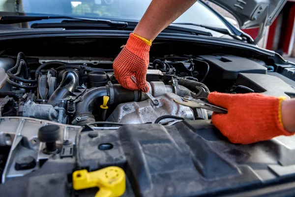 Human hands with wrenches in protective gloves upon car engine