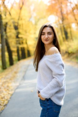 Kadın portresi. Güz ormanında sarı yapraklarla poz veren gündelik giysili genç bir kadın.